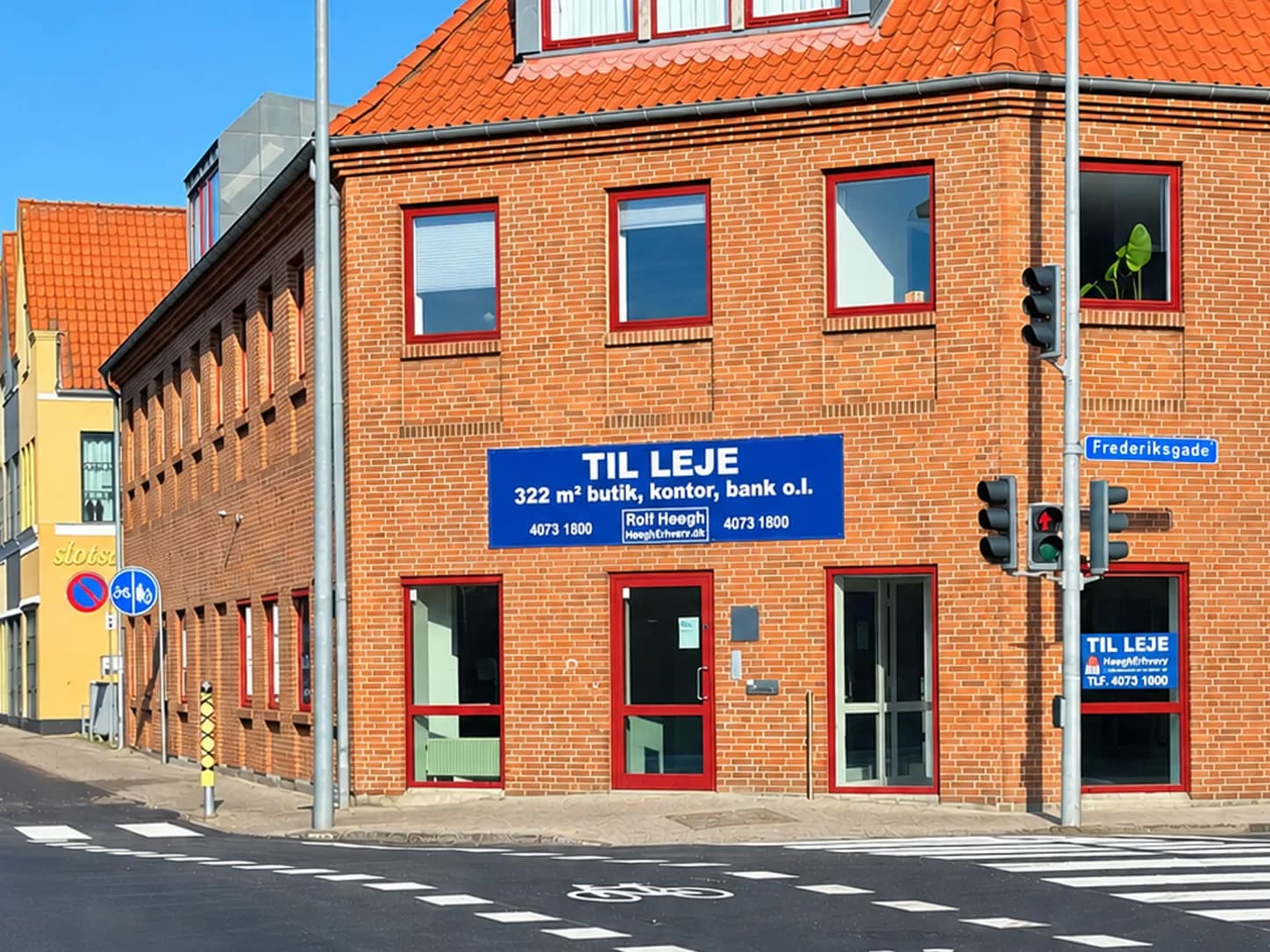 Hjørneejendommens nyrenoverede facade i røde mursten med røde vinduer og et blåt Til leje-skilt over indgangen mod Frederiksgade